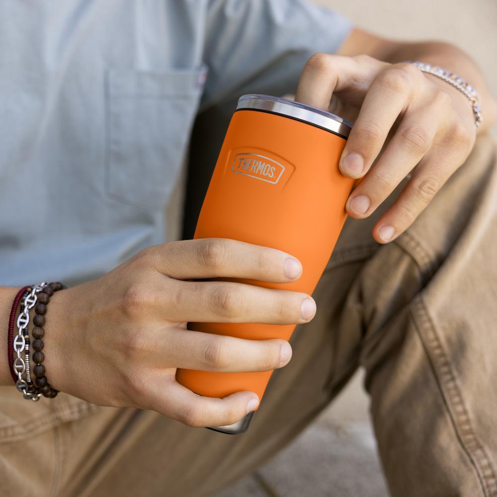 Person holding an orange Thermos insulated travel tumbler with a neutral background